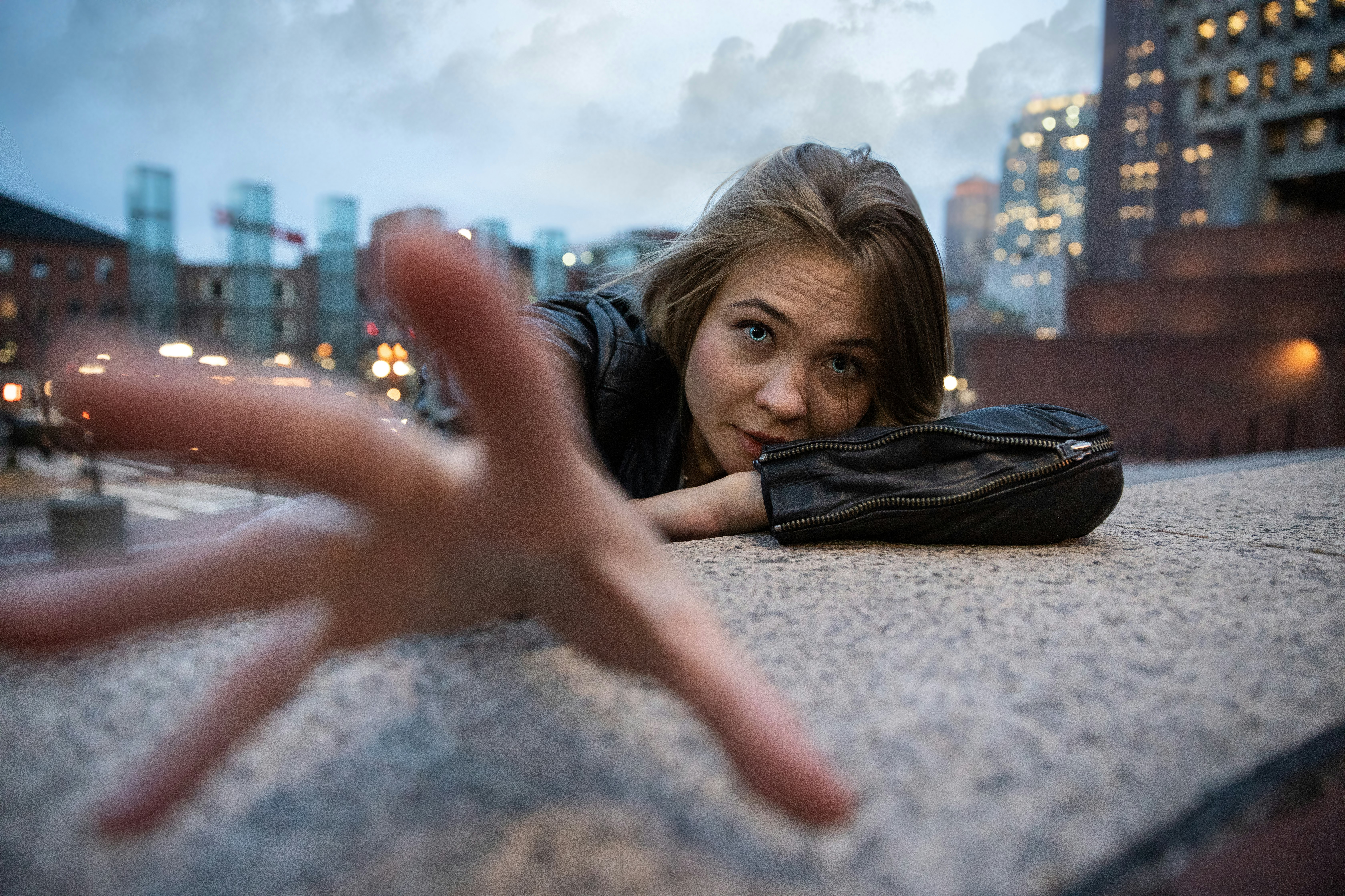 woman wearing black leather jacket leaning on gray concrete surface while right hand about reach